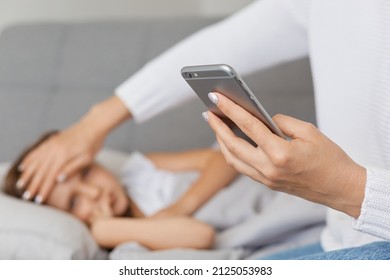 Horizontal shot of sick little girl with high temperature, having fever, suffering headache, faceless sitting near kid with cell phone in hands and calling doctor. - Powered by Shutterstock