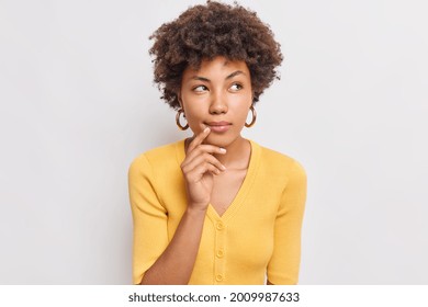 Horizontal shot of thoughtful young African American woman looks aside has dreamy expression interesting idea in mind wears casual yellow jumper isolated over white background makes decision - Shutterstock ID 2009987633