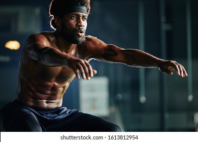 Horizontal shot of topless African American man doing squat exercise in gym