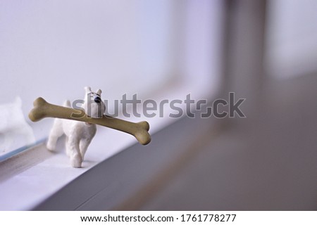 A horizontal shot of a toy dog holding a huge bone on a blurred background