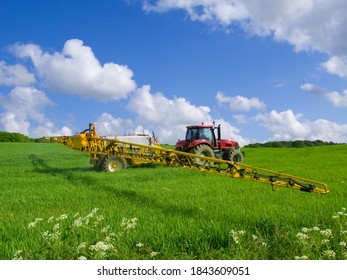 Horizontal shot of a tractor working in a green field with a cloudy sky overhead on a sunny day with copy space. - Shutterstock ID 1843609051