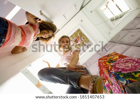 Horizontal shot of two ecstatic young women with one trying on shoes in a shop seen from below.