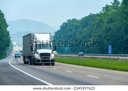 Horizontal shot of a white box truck changing lanes on an interstate highway.