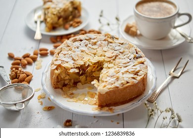 Horizontal Shot Of A Whole Round Delicious Apple Cake Tart With Almond Flakes Served On Wooden Table. With Coffee In A Cup And Slice Of A Pie On Soucer.