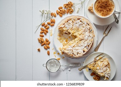 Horizontal shot of a whole round delicious apple cake tart with almond flakes served on wooden table. With coffee in a cup and slice of a pie on soucer.