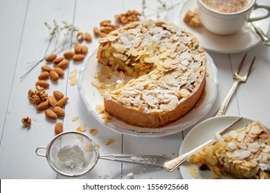 Horizontal shot of a whole round delicious apple cake tart with almond flakes served on wooden table. With coffee in a cup and slice of a pie on soucer.