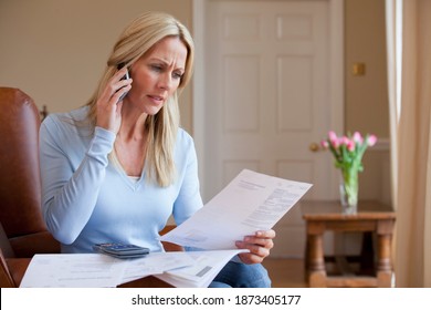 Horizontal shot of a woman in an armchair talking on a mobile phone holding bills at home. - Powered by Shutterstock