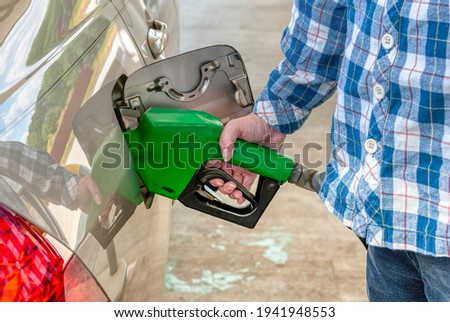 Horizontal shot of a woman from the right below shoulders down pumping gas into her car.