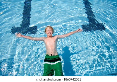 Horizontal Shot Of A Young Boy In Swimming Trunks Floating In A Swimming Pool.