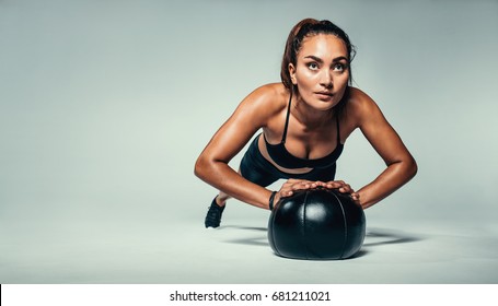 Horizontal shot of young fit woman doing push up on medicine ball. Fitness female exercising with a medicine ball on grey background. - Powered by Shutterstock