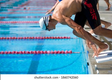 Horizontal Shot Of A Young Man On Starting Block About To Dive In A Pool For Swimming Competition.