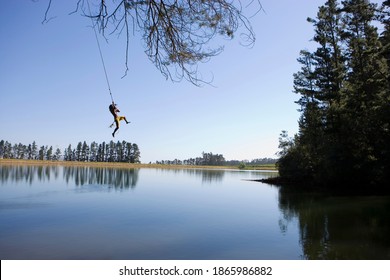 Horizontal shot of a young man swinging off a rope above the lake on a sunny day with copy space.