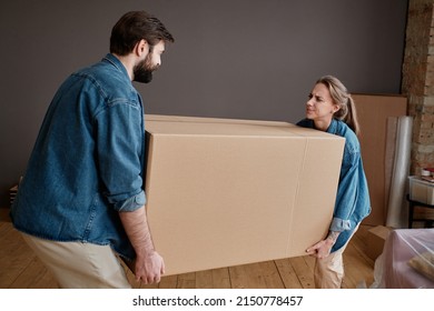 Horizontal Shot Of Young Man And Woman Moving To New Apartment Carrying Big Heavy Box Together