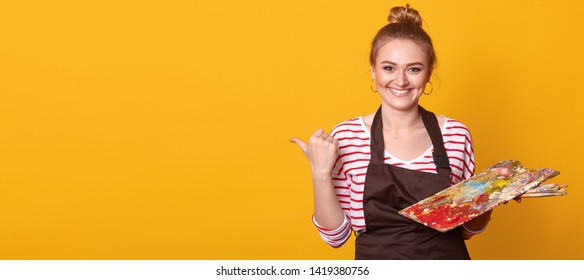 Horizontal shot of young smiling blonde woman artist isolated over yellow studio background, holding brushes and palette of colours. Paintings and art equipment concept. Copy space for promotion text. - Powered by Shutterstock