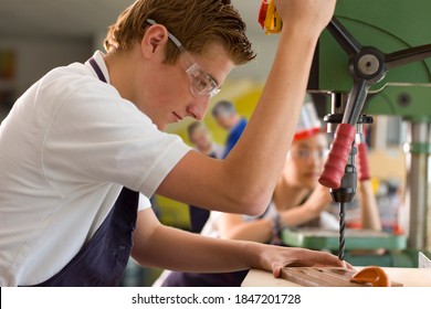 A horizontal side view of a serious student wearing safety glasses while using the drill machine in a vocational school - Shutterstock ID 1847201728