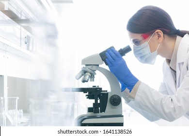 Horizontal side view shot of unrecognizable female medical scientist examining specimen using microscope in modern laboratory