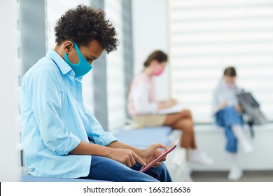 Horizontal Side View Shot Of Unrecognizable Boy Wearing Mask Playing Mobile Games While Sitting In Queque To School Medical Room, Copy Space