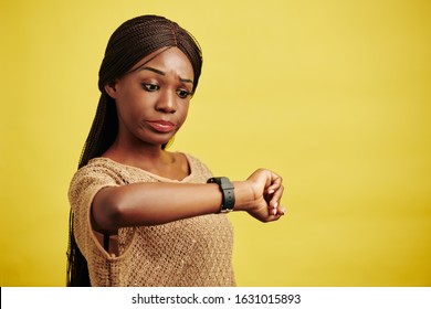 Horizontal Studio Portrait Of Black Woman Getting Late For Something Checking Time, Yellow Background