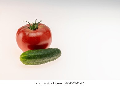 Horizontal studio still life of a red tomato and cucumber placed closely together and centered on a white background. The closer arrangement compared to the wider composition version gives a more intimate pairing with copy space on the sides. Suitable for healthy eating campaigns, fresh food editorial, vegetable brand advertising, recipe platforms, and commercial food photography. No people, clean white background.