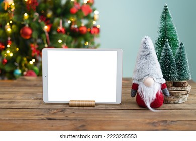 Horizontal tablet mockup on wooden table with Christmas decoration. Gnome and Christmas tree. Space to place text on the tablet screen.