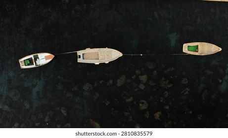 Horizontal top down drone view of three moored boats aligned over a dark rocky seabed near Naples.