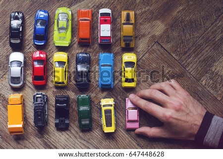 horizontal top view of male hand arranging an assorted metal colorful toy car collection on brown wooden floor in natural light
