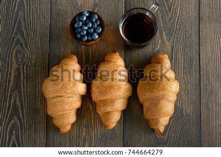 Horizontal top view shot of three freshly baked croissants just from the oven small bowl of blueberries and a cup of tea on the table food composition breakfast hunger tasty healthy meal.