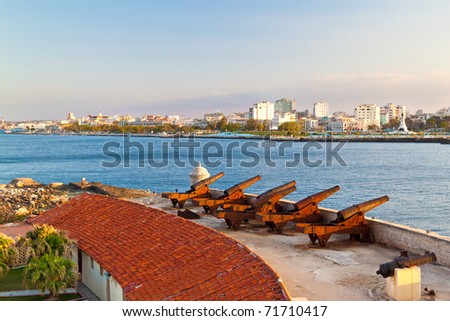 Horizontal view of a battery of cannons facing the bay of Havana with a view of the old city