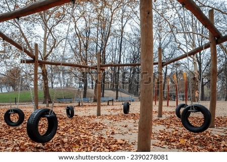 Horizontal view of big empty playground tire swing in a public park, with autumn foliage. Public playground, playpark, or play area with games for kids and many red fall leaves on the ground.