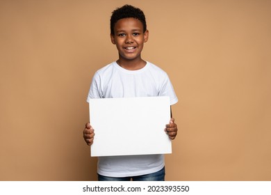 Horizontal view of the cheerful multiracial boy holding a blank white sheet of paper and looking at the camera with toothy smile. Space for text, advertising  - Powered by Shutterstock