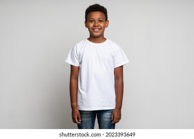 Horizontal view of cute little boy with stylish curly hairdo in white T-shirt standing and looking at camera with happy face. Indoor studio shot isolated on white background  - Powered by Shutterstock