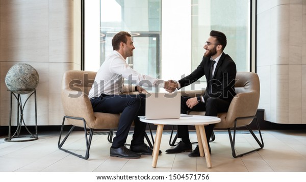 Horizontal view european and arabian businessmen\
in formal wear accomplish meeting shaking hands feels satisfied\
after negotiations, HR manager greeting applicant before job\
interview process\
concept
