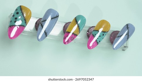 Horizontal view of five artificial nails showcasing creative ragdoll patchwork patterns in vibrant colors with hand painted stitching details