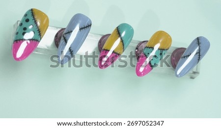 Horizontal view of five artificial nails showcasing creative ragdoll patchwork patterns in vibrant colors with hand painted stitching details
