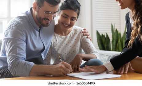 Horizontal view happy married couple Caucasian husband Indian ethnicity wife signing rental contract at meeting with realtor or landlord, first property purchase, mortgage and loan ownership concept
