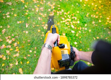 A Horizontal View Of Male Hands Using A Cordless, Electric Leaf Blower In A Garden. Garden Works. Autumn, Fall Gardening Works In A Backyard, On A Lawn, Grass.