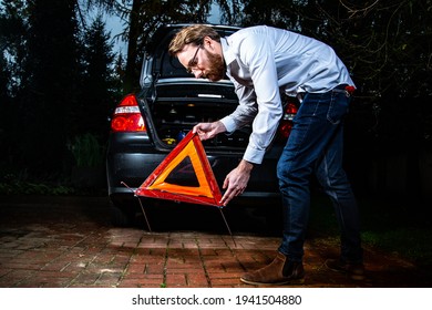 Horizontal view of a man setting up an emergency warning triangle behind a car. A road accident, a car breakdown, emergency situation.