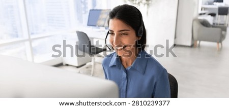 Horizontal view smiling operator, call center worker in headset working in office using computer, assists clients and responds to inquiries. Customers support services workflow, digital communication