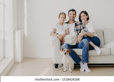 Horizontal view of three friendly family members and small pedigree dog pose at camera for making memorable photography. Dauther spends free time with mother and father, have good day at home
