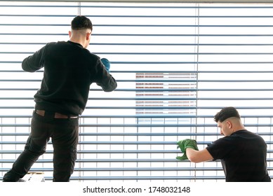 Horizontale Sicht auf zwei männliche professionelle Reiniger, die Jalousien auf einer großen Fensterfront mit Mikrofasertuch reinigen