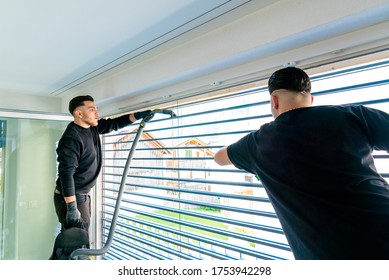 Horizontale Sicht auf zwei männliche professionelle Reiniger, die Jalousien auf einer großen Fensterfront mit Mikrofasertuch reinigen