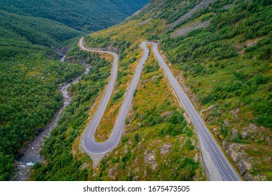 Horizontal view of winding road with sharp bends along the foot of mountain with a small river alongside the road. Colourful green covered mountains. Ultimate roadtrip destination, Norway Scandinavia.