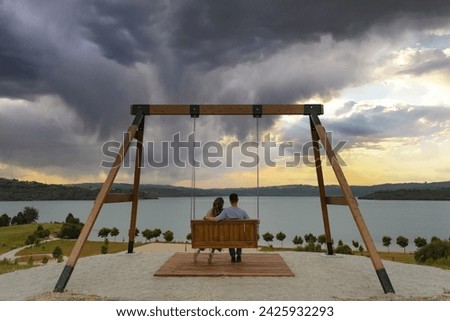 Horizontal view of young couple at sunset on a cloudy day sitting on a wooden swing overlooking the sea in As Pontes de Garcia Rodriguez, A Coruña, Galicia.
