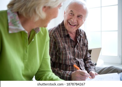 Horizontal Waist Up Portrait Of A Senior Couple Smiling At Each Other With Man Signing Paperwork Indoors.