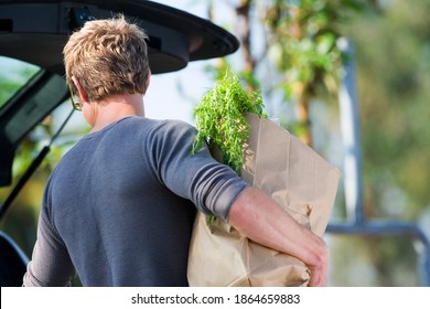 Horizontal Waist Up Rear View Of A Man Loading Groceries Into A Car's Boot In A Supermarket's Car Park.