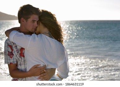 Horizontal waist up rear view of a teenage couple in a passionate hug on the beach with copy space.