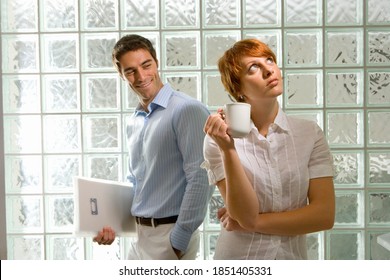 Horizontal Waist Up Shot Of A Businessman Admiring A Female Colleague Holding A Mug Thinking By A Glass Block Wall In Office.