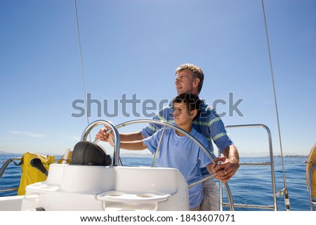 Horizontal waist up shot of a father and son steering a boat on a clear sunny day with copy space.