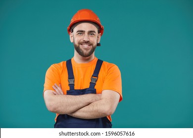 Horizontal waist up studio portrait of cheerful man wearing hardhat and workwear standing with atms crossed looking at camera