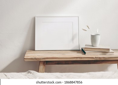 Horizontal white frame mockup on vintage wooden bench, table. Ceramic mug with dry Lagurus ovatus grass and books. White wall background. Scandinavian interior room design. Selective focus.
